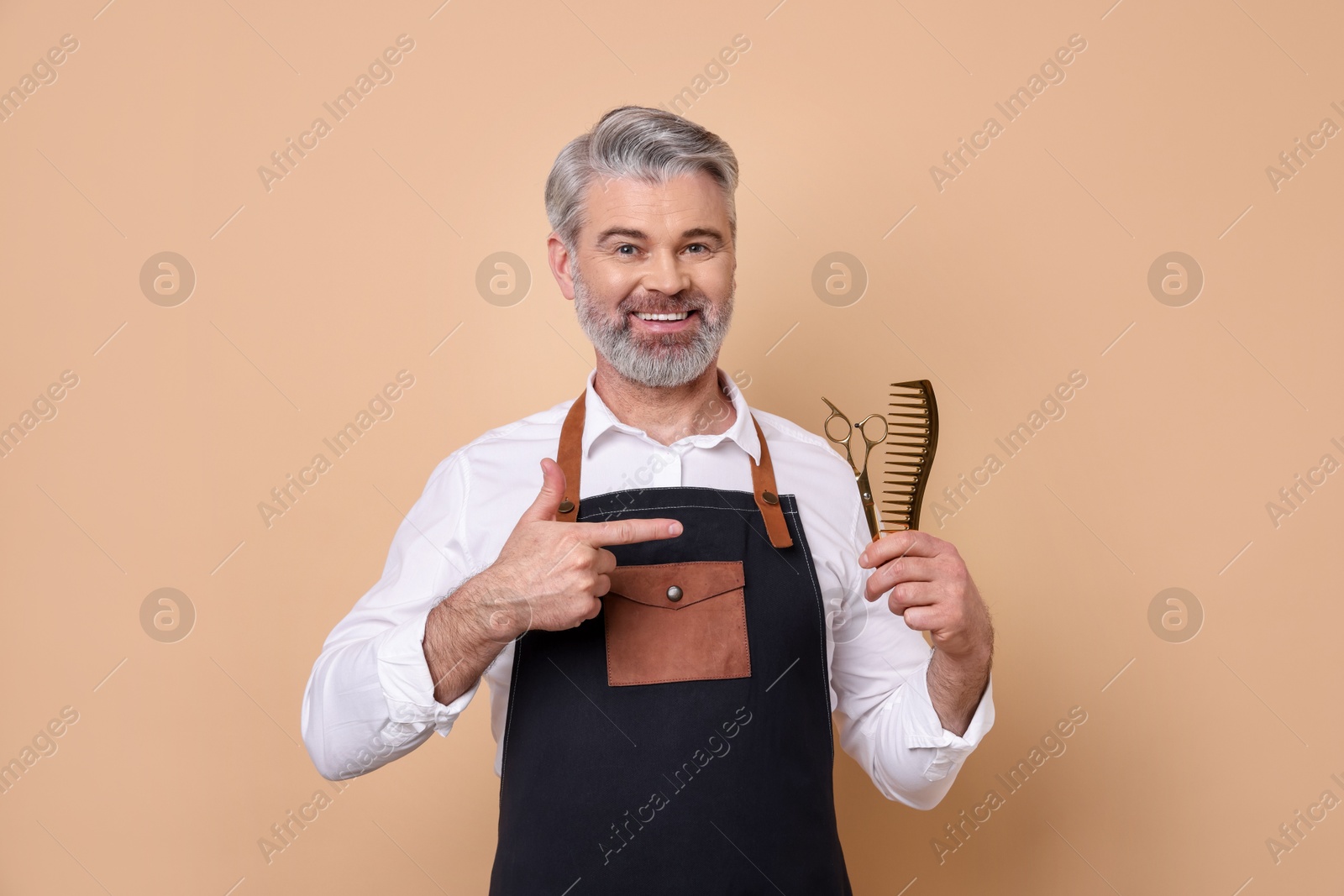 Photo of Smiling hairdresser with scissors and comb on beige background