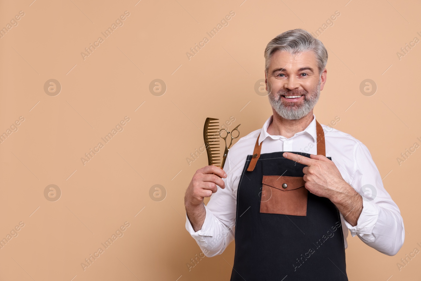 Photo of Smiling hairdresser with scissors and comb on beige background, space for text