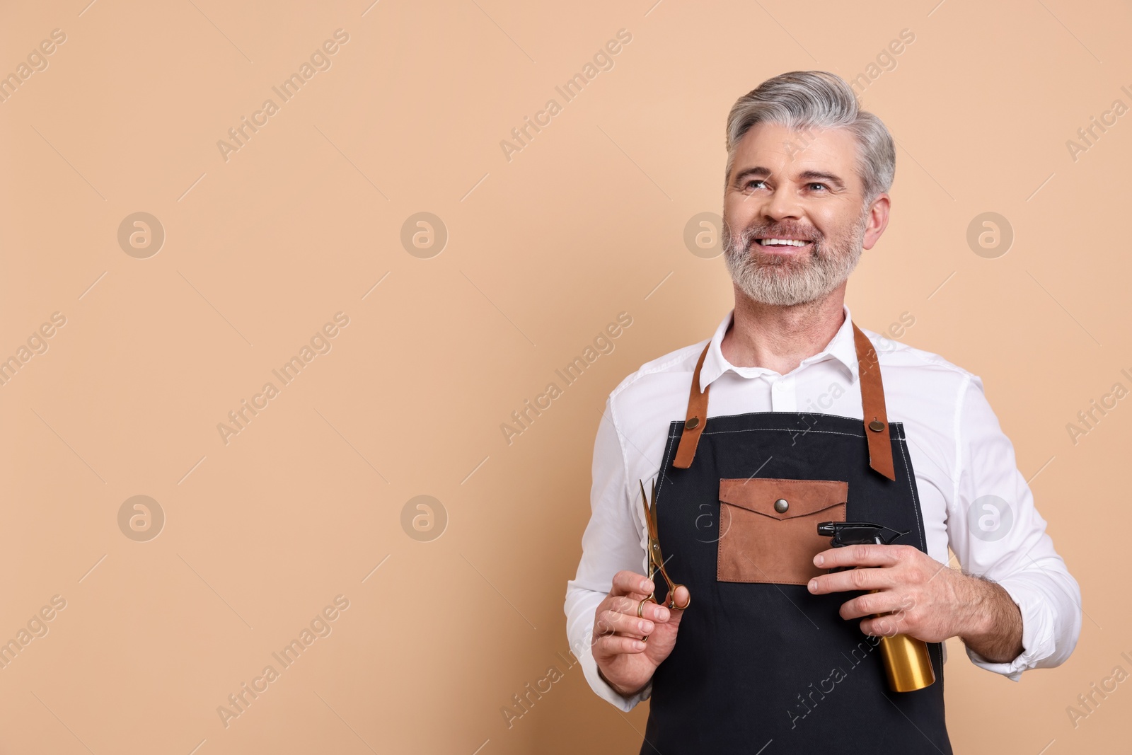 Photo of Smiling hairdresser with scissors and spray bottle on beige background, space for text