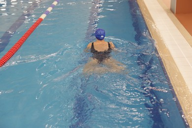 Photo of Woman wearing swimsuit and cap swimming in pool indoors