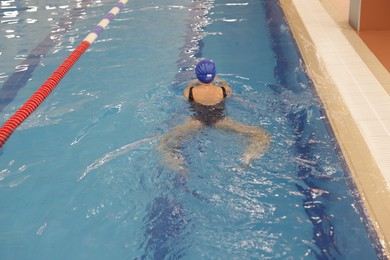 Photo of Woman wearing swimsuit and cap swimming in pool indoors