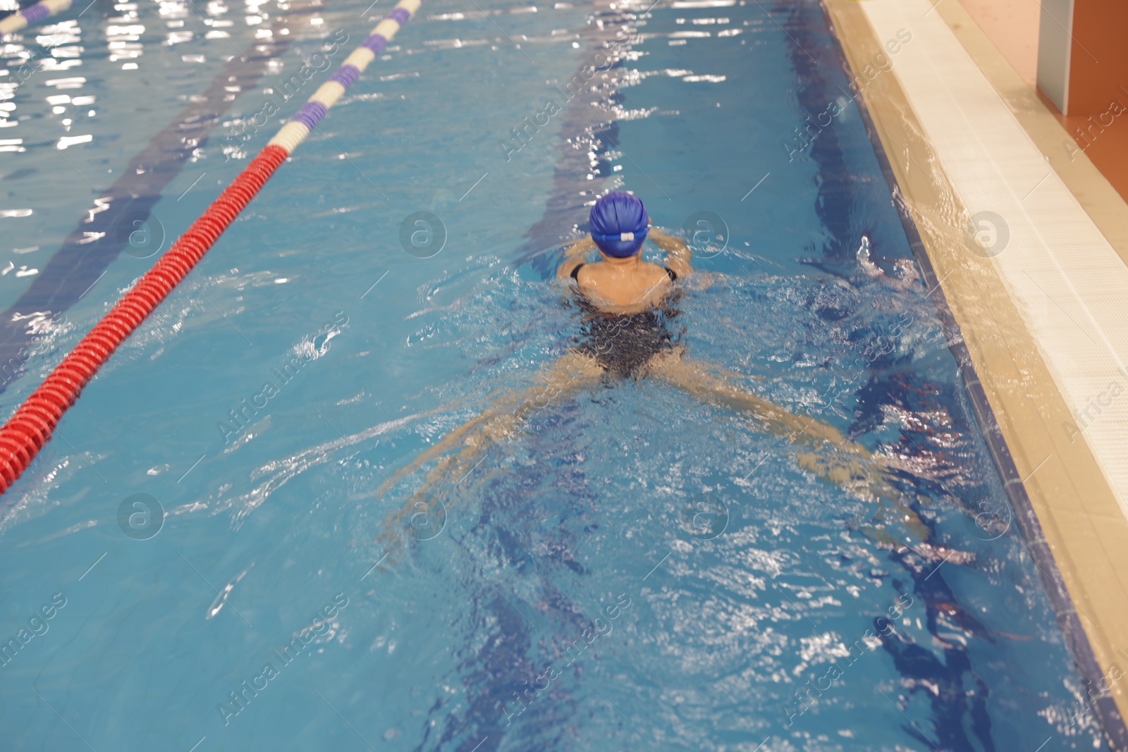 Photo of Woman wearing swimsuit and cap swimming in pool indoors