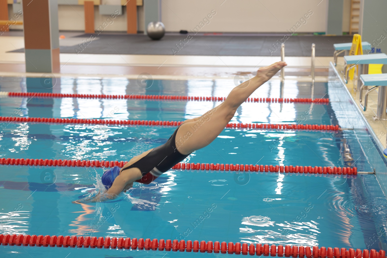 Photo of Sporty woman in swimsuit and cap jumping into swimming pool indoors