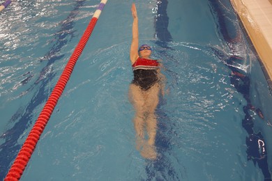 Sporty woman wearing cap and goggles swimming in pool indoors