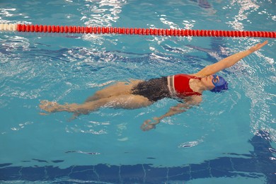 Sporty woman wearing cap and goggles swimming in pool indoors