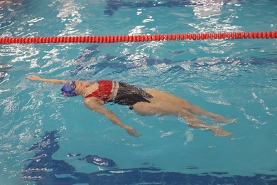 Sporty woman wearing cap and goggles swimming in pool indoors