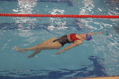 Photo of Sporty woman wearing cap and goggles swimming in pool indoors