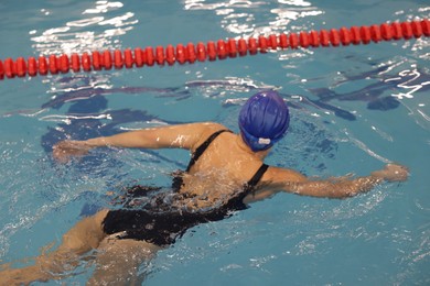 Woman wearing swimsuit and cap swimming in pool indoors