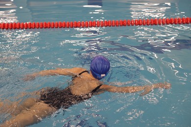 Photo of Woman wearing swimsuit and cap swimming in pool indoors