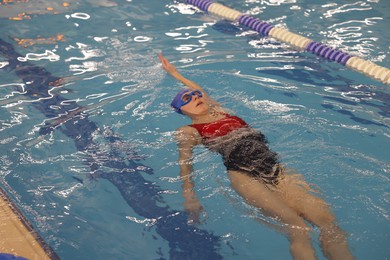 Woman wearing swimsuit, cap and goggles swimming in pool indoors