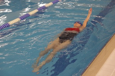 Woman wearing swimsuit, cap and goggles swimming in pool indoors