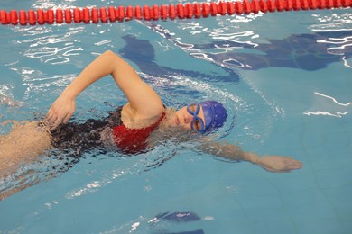 Sporty woman wearing swimsuit, cap and goggles swimming in pool indoors