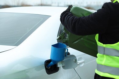 Photo of Man pouring fuel from canister into funnel outdoors, closeup