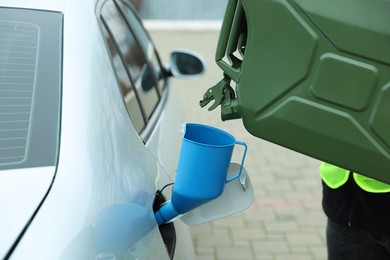 Photo of Man pouring fuel from canister into funnel outdoors, closeup