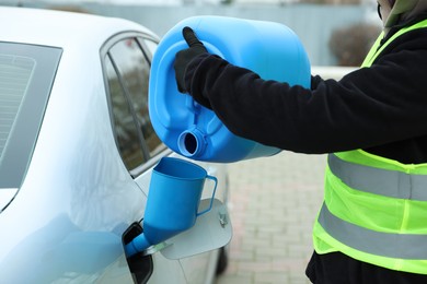 Photo of Man pouring fuel from canister into funnel outdoors, closeup