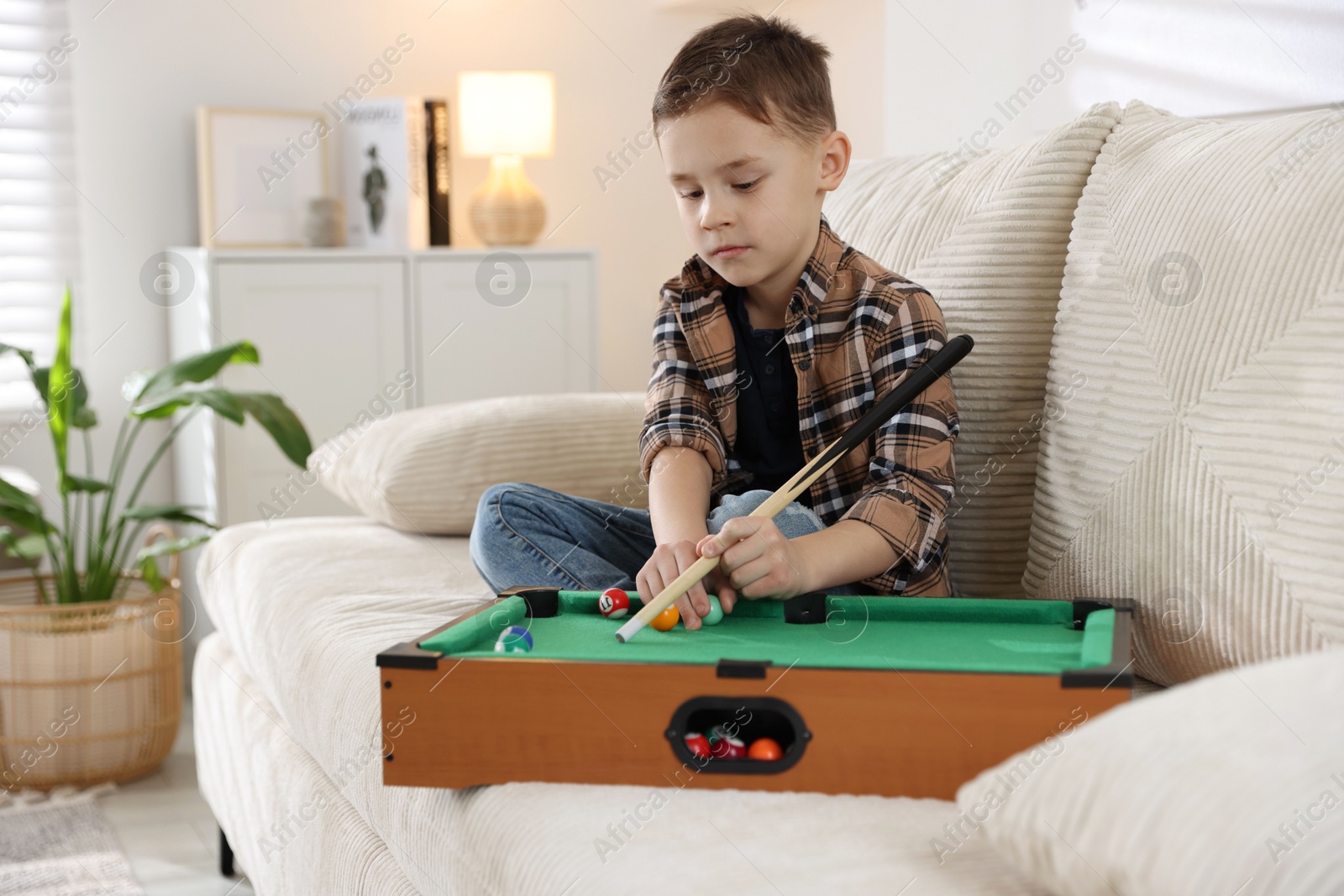 Photo of Cute little boy playing billiards at home