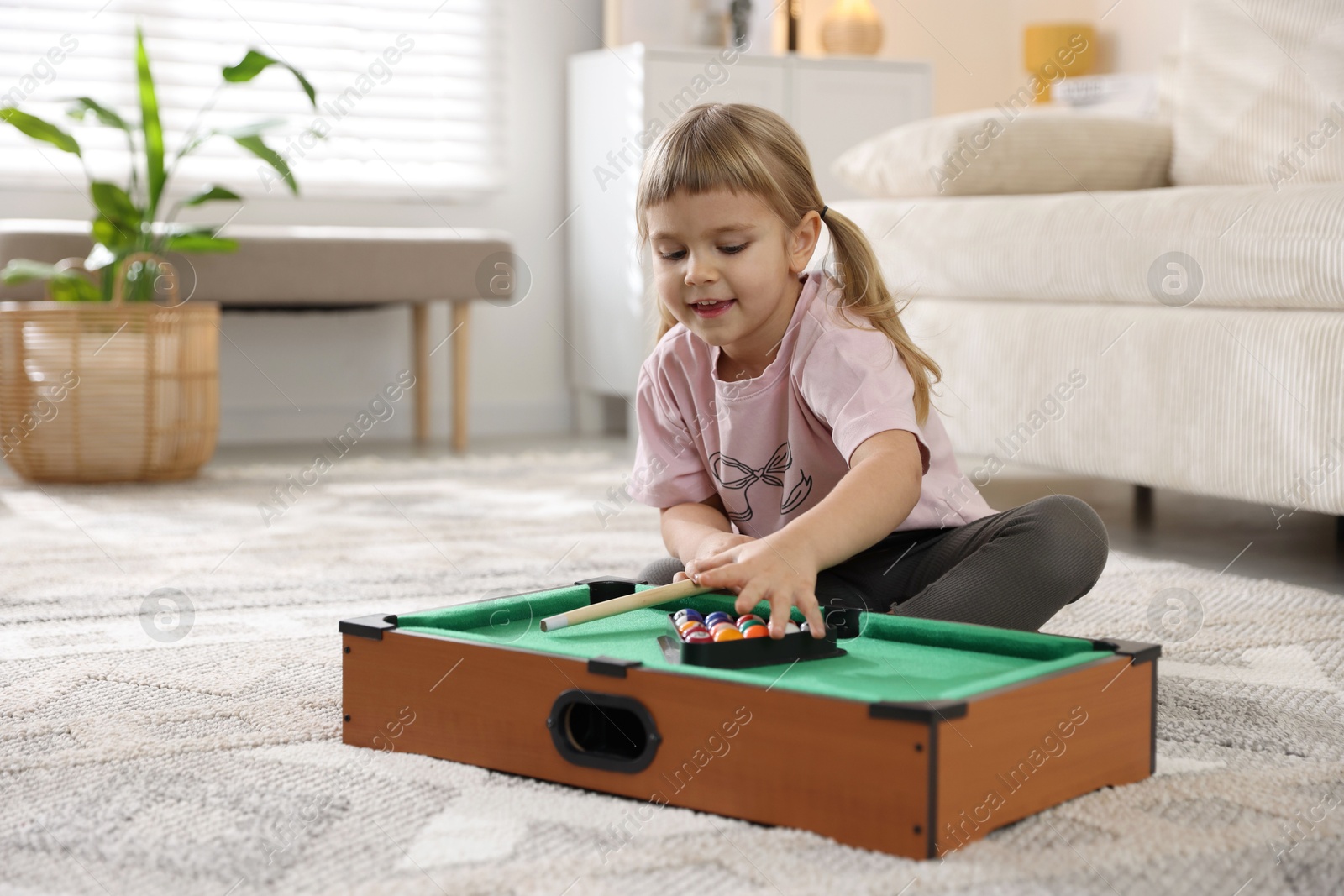 Photo of Cute little girl playing billiards at home