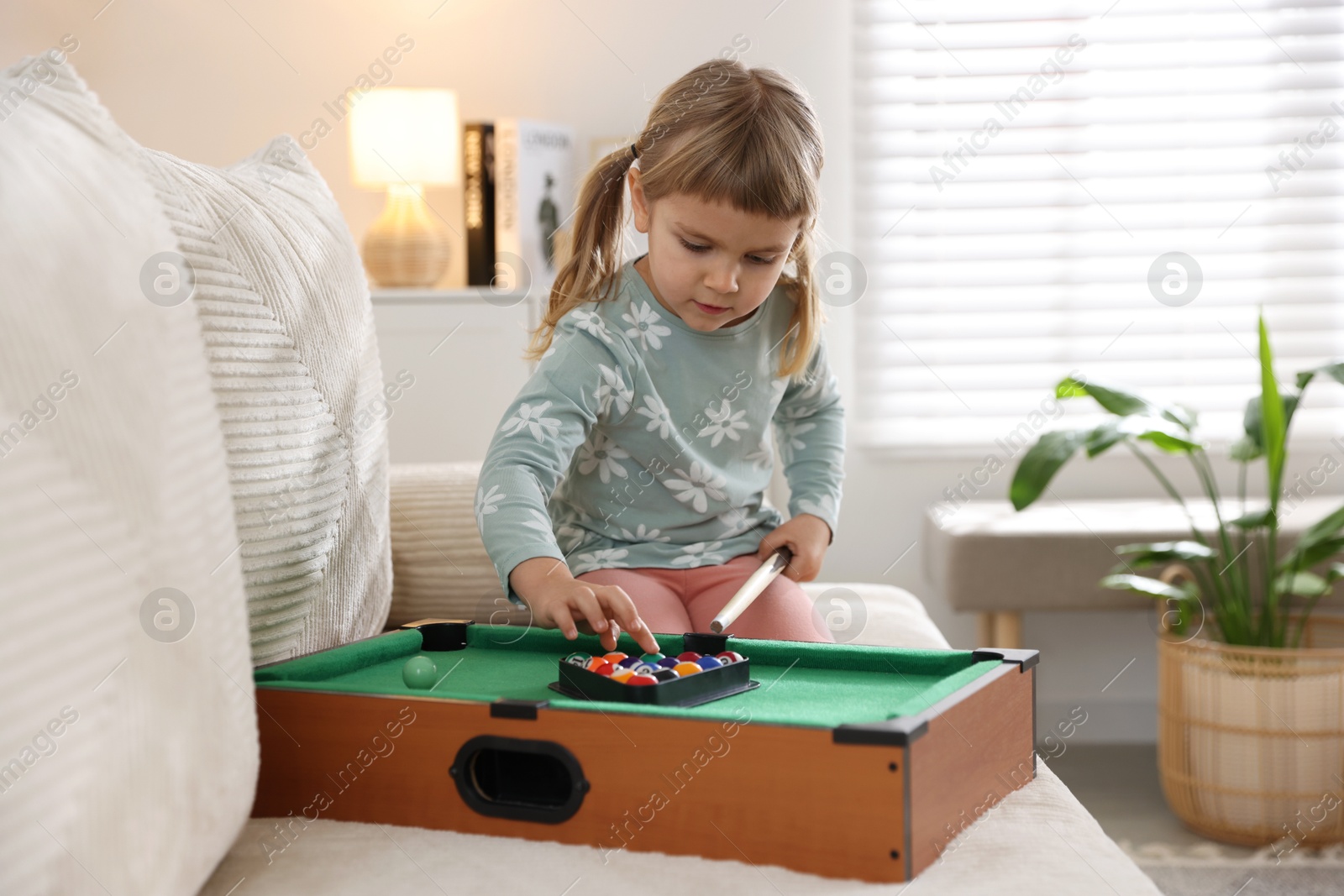 Photo of Cute little girl playing billiards at home