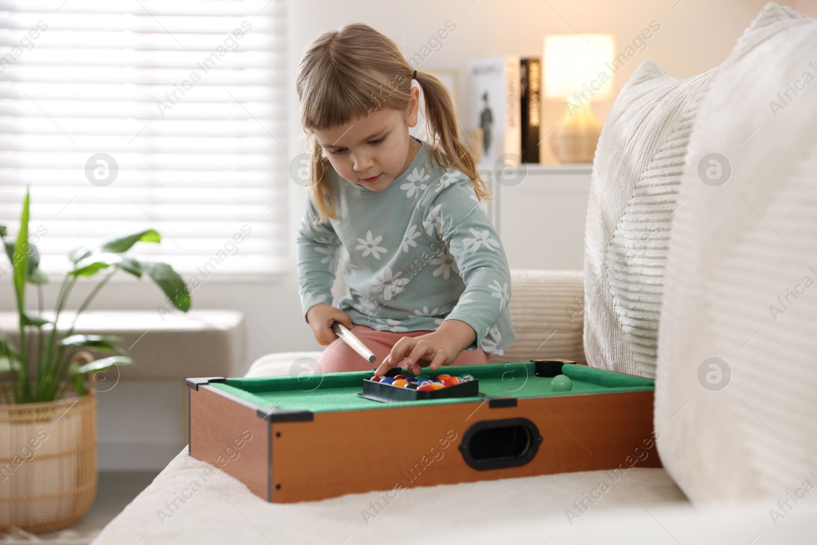 Photo of Cute little girl playing billiards at home