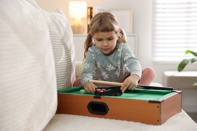 Photo of Cute little girl playing billiards at home