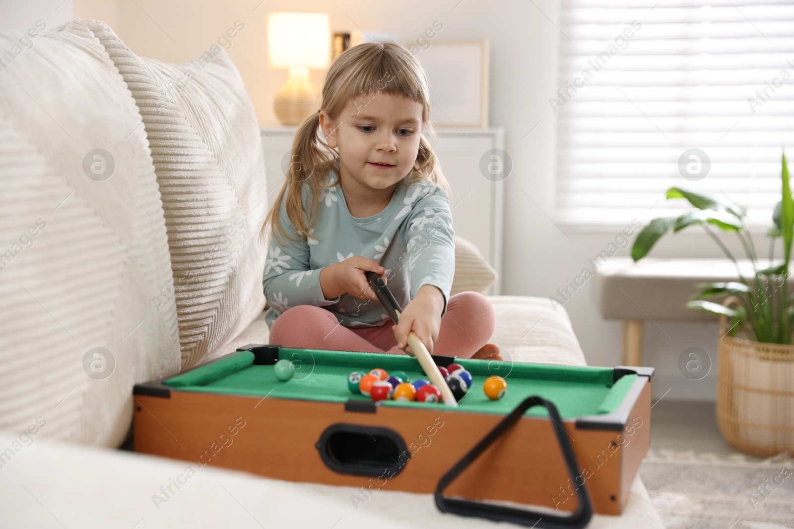 Photo of Cute little girl playing billiards at home