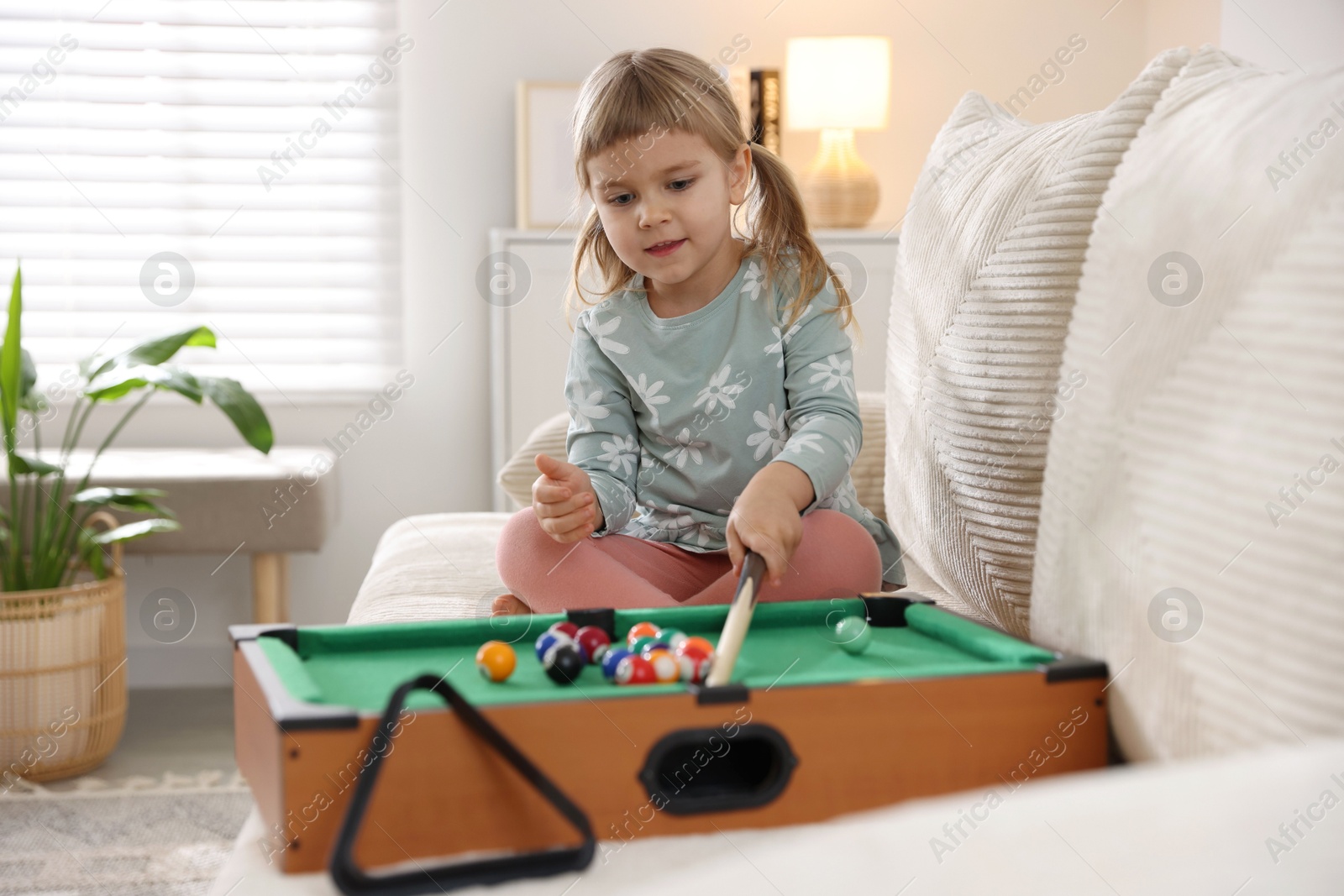 Photo of Cute little girl playing billiards at home