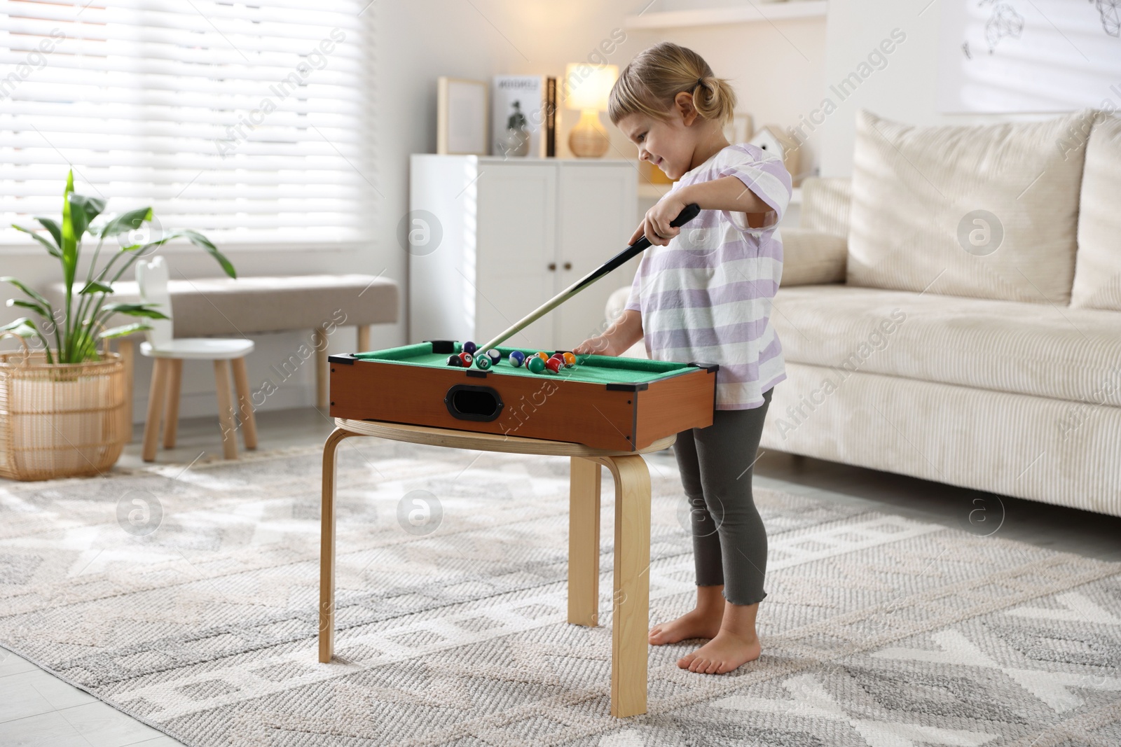 Photo of Cute little girl playing billiards at home