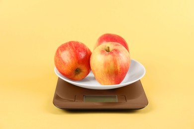 Photo of Electronic kitchen scale with apples on yellow background