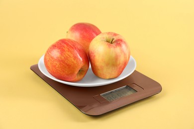 Photo of Electronic kitchen scale with apples on yellow background, closeup