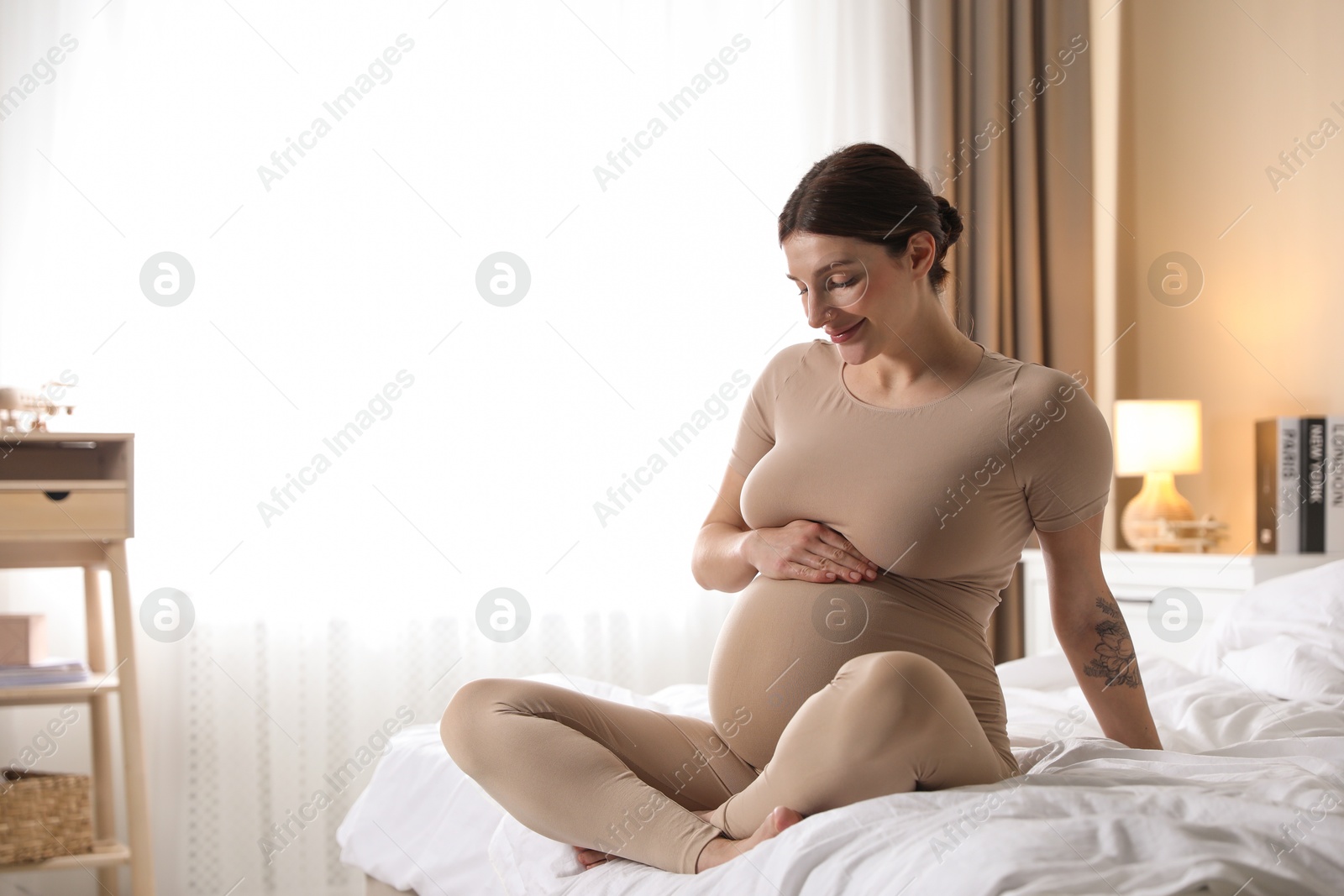 Photo of Beautiful pregnant woman on bed at home. Space for text