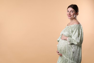 Photo of Beautiful pregnant woman with cute belly on beige background. Space for text