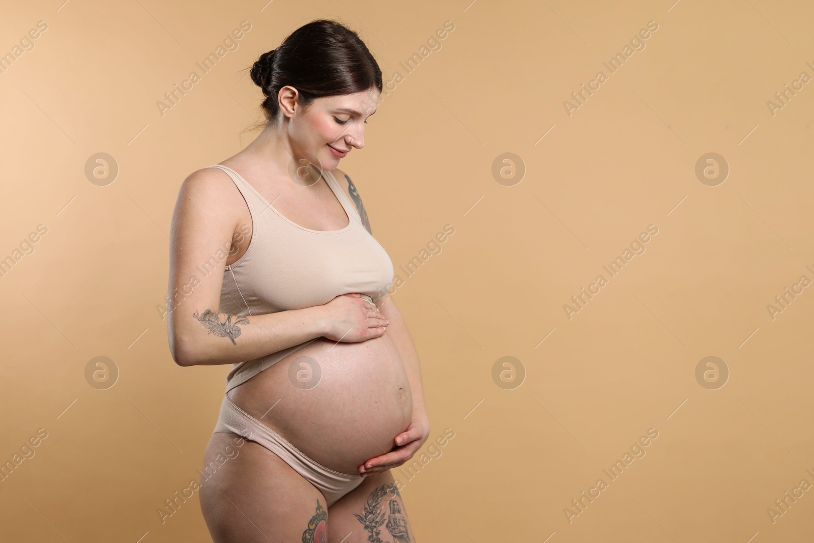 Photo of Beautiful pregnant woman with cute belly on beige background. Space for text