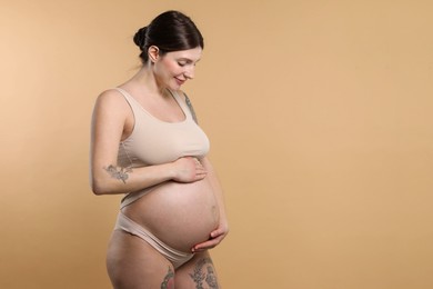 Beautiful pregnant woman with cute belly on beige background. Space for text