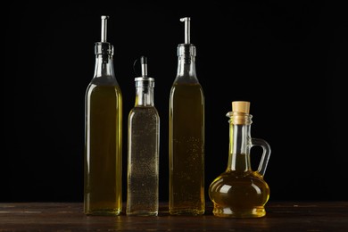 Photo of Oils and vinegar in bottles on wooden table against black background