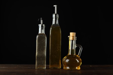 Photo of Oils and vinegar in bottles on wooden table against black background