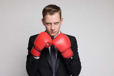 Competition. Businessman in suit wearing boxing gloves on grey background