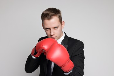 Competition. Businessman in suit wearing boxing gloves on grey background