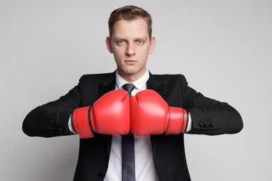 Competition. Businessman in suit wearing boxing gloves on grey background