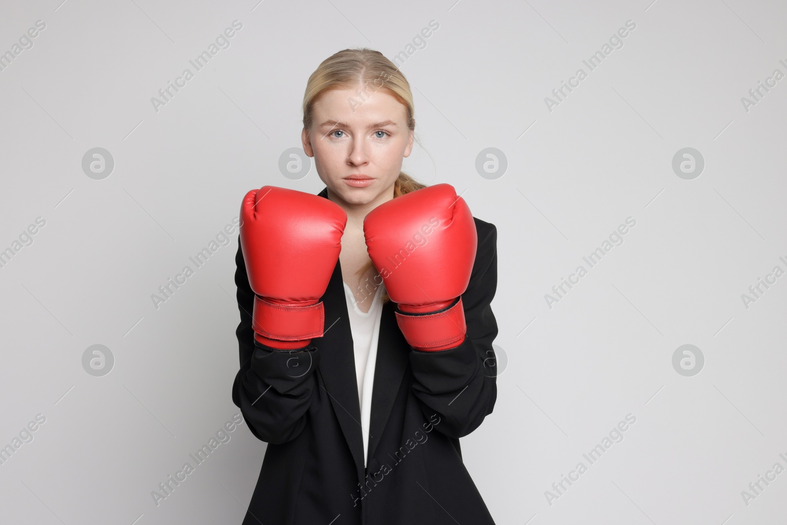 Photo of Competition. Businesswoman in suit wearing boxing gloves on grey background