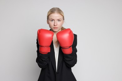 Photo of Competition. Businesswoman in suit wearing boxing gloves on grey background