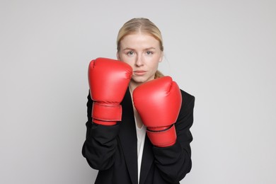 Photo of Competition. Businesswoman in suit wearing boxing gloves on grey background