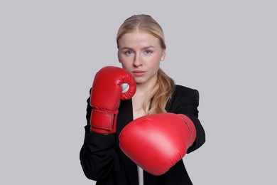 Photo of Competition. Businesswoman in suit wearing boxing gloves on grey background