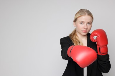 Competition. Businesswoman in suit wearing boxing gloves on grey background. Space for text