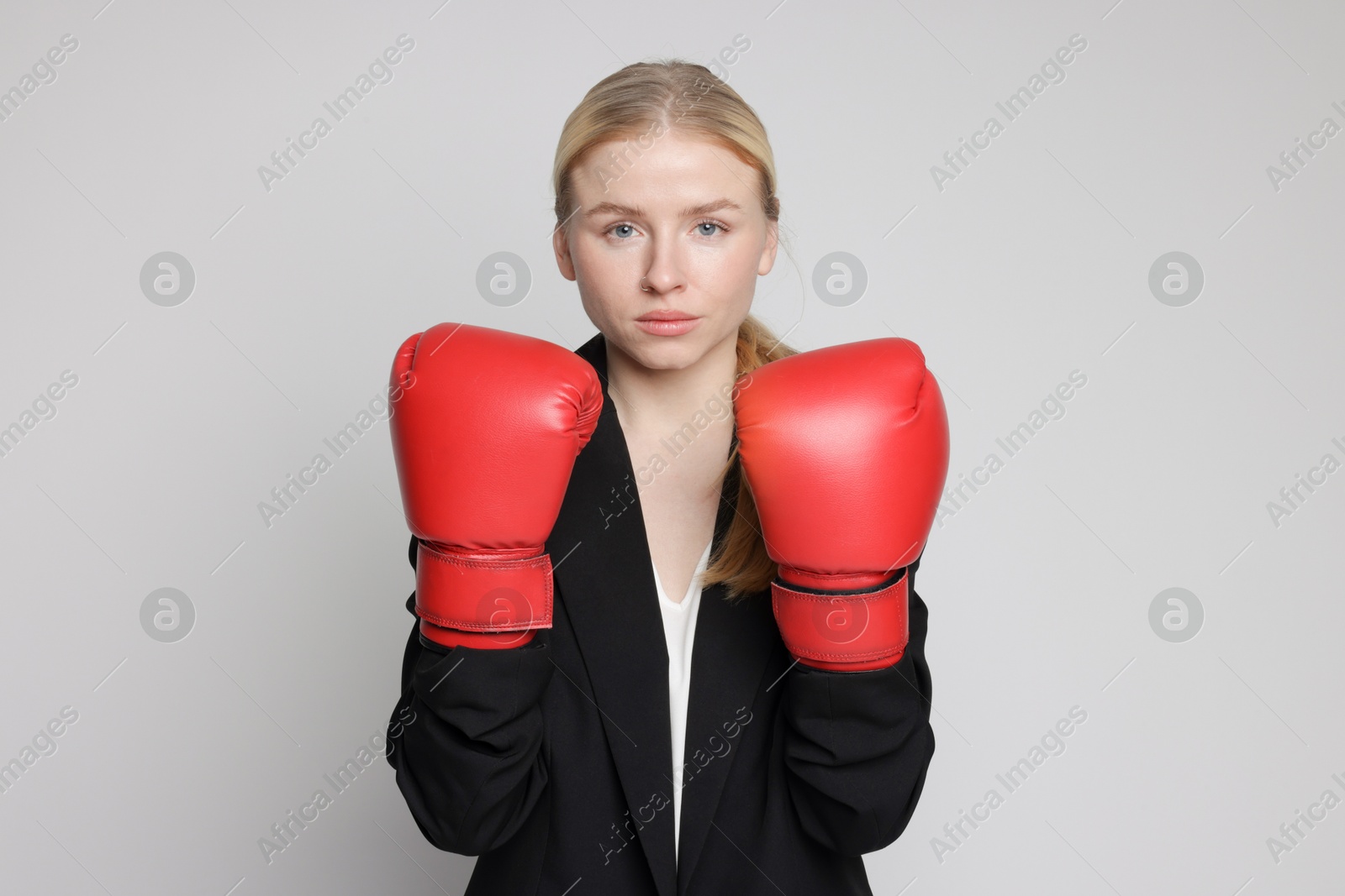 Photo of Competition. Businesswoman in suit wearing boxing gloves on grey background