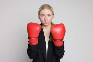 Photo of Competition. Businesswoman in suit wearing boxing gloves on grey background