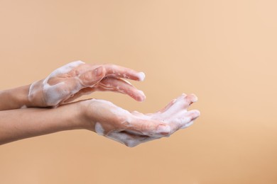 Photo of Woman washing hands with foaming soap on beige background, closeup. Hygiene