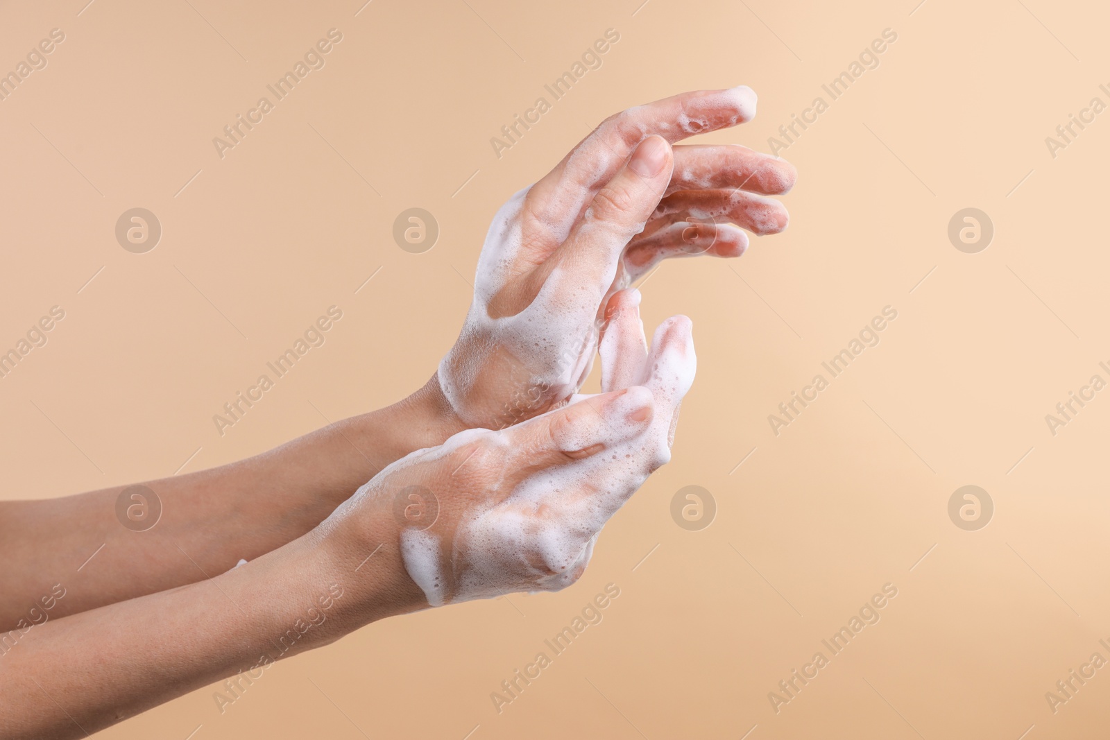 Photo of Woman washing hands with foaming soap on beige background, closeup. Hygiene