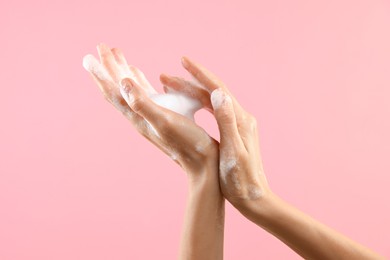 Photo of Woman washing hands with foaming soap on pink background, closeup. Hygiene