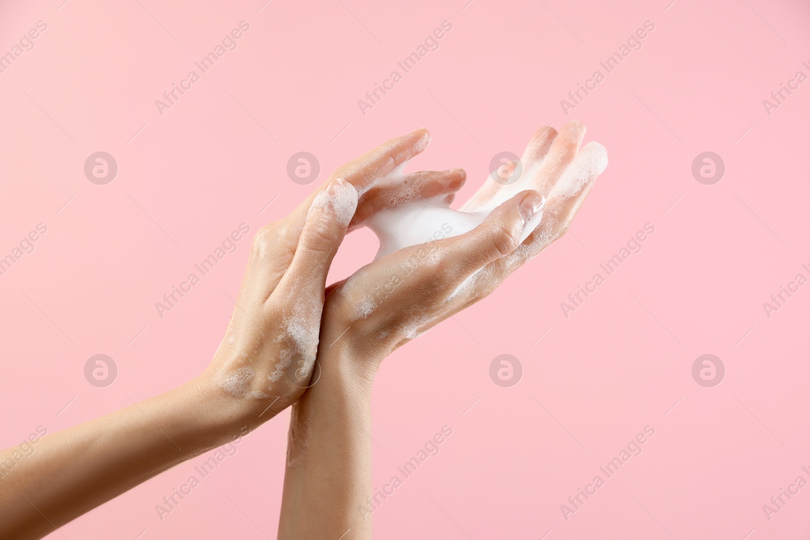 Photo of Woman washing hands with foaming soap on pink background, closeup. Hygiene