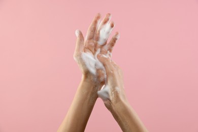 Woman washing hands with foaming soap on pink background, closeup. Hygiene